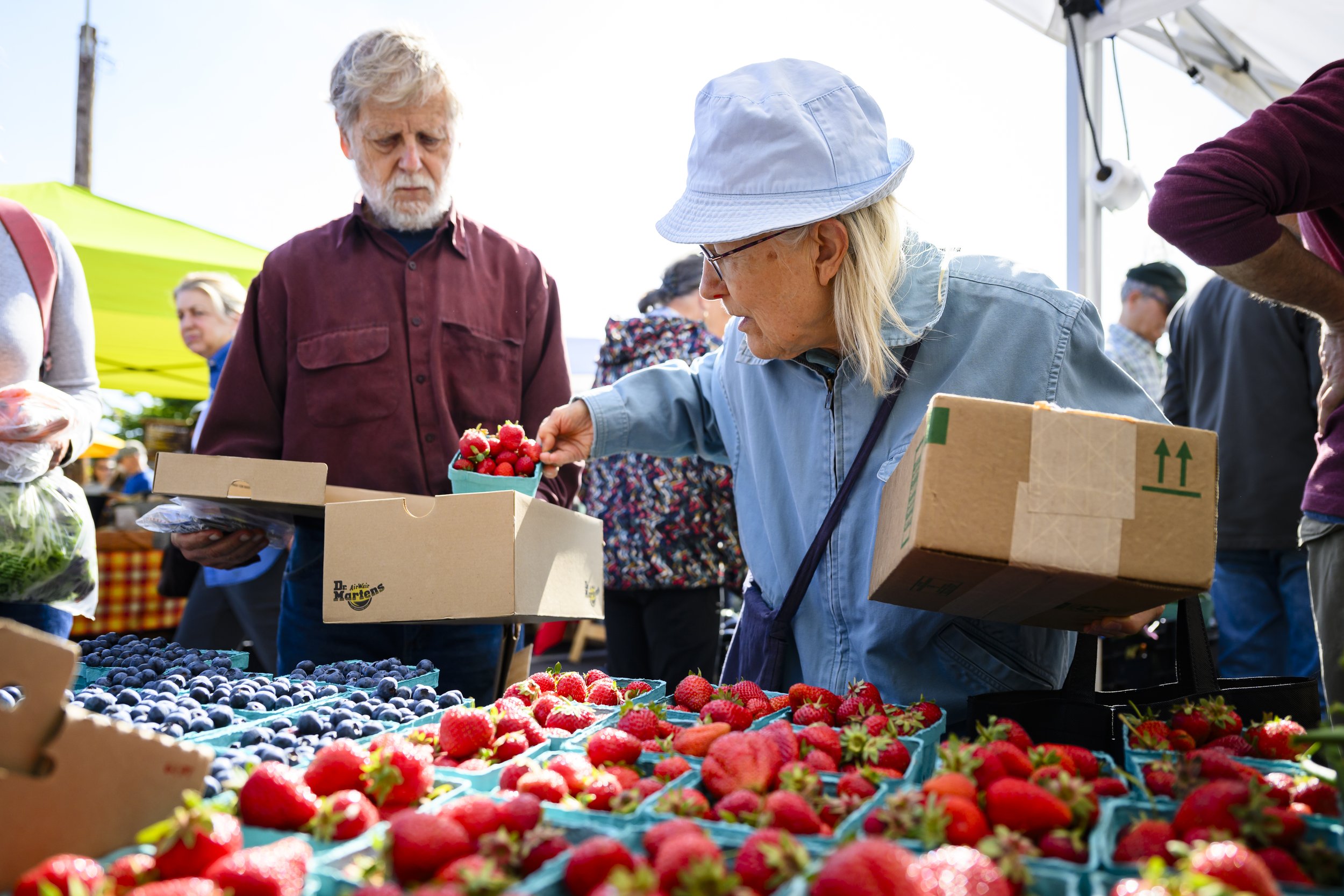   Judy Dobkevich hands fresh strawberries to her husband, Michael Dobkevich, at the Port Townsend Farmers Market. The Dobkevichs use food access programs to help supply their pantry with fresh fruit and vegetables. Photo by Heather Johnson  