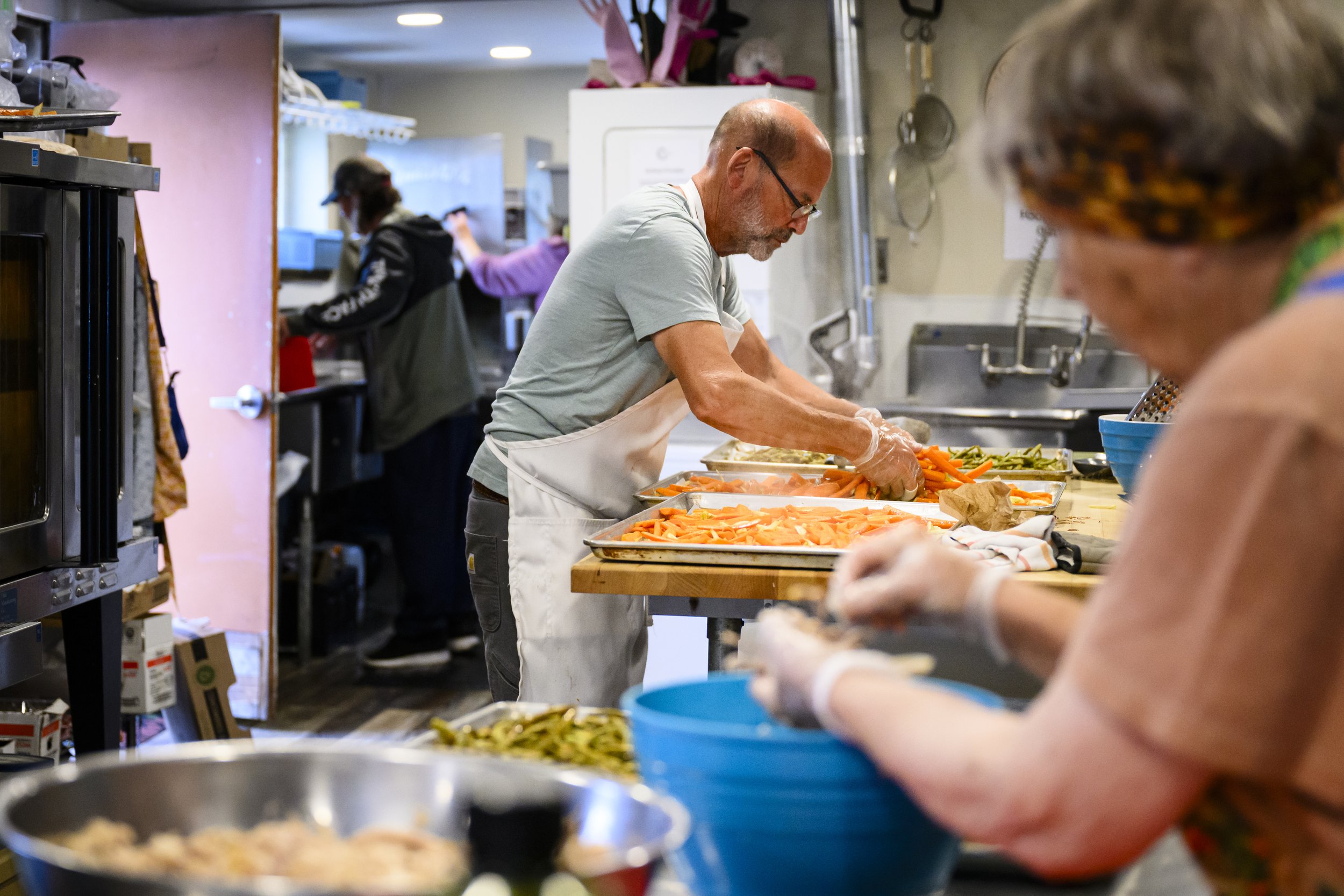   Steve Levi (left) and Kathy Ryan volunteer at the Recovery café, cooking free meals for community members. They source ingredients from local farms when possible. Photo by Heather Johnson  