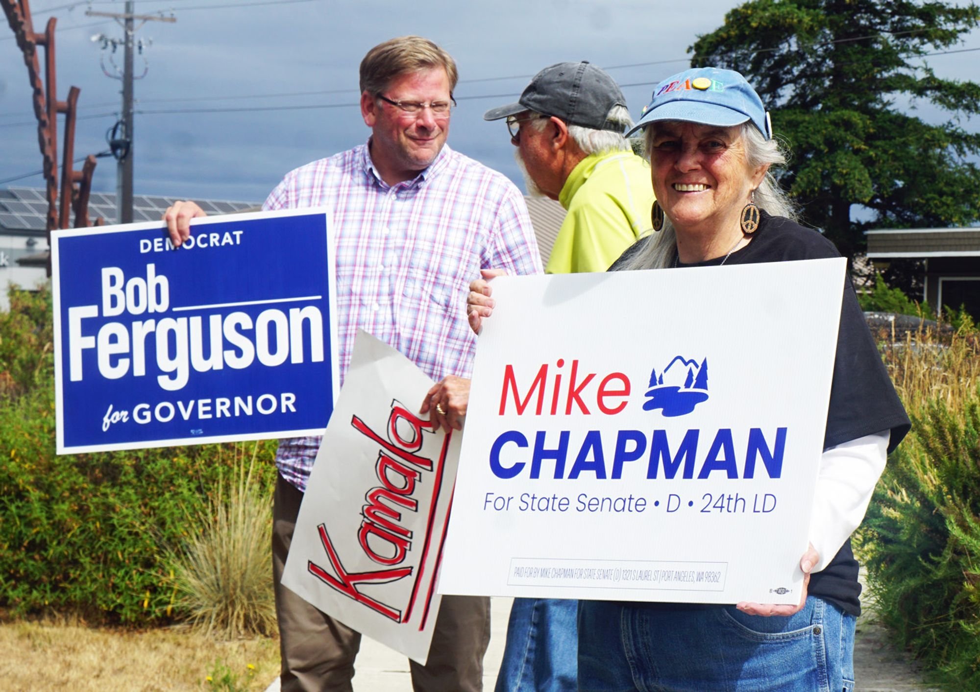   State Senate Candidate Mike Chapman (left) talks to a constituent as Julia Cochrane waves a sign to support him.  