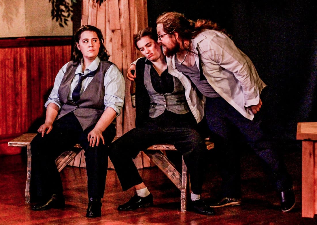 Three actors gathered conspiratorially on a bench