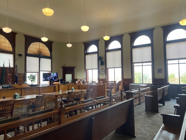 Brown wooden tables and a banister in front of a jury box and judge's bench. 